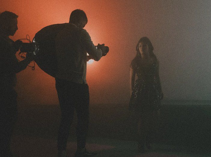 Silhouetted camera operators filming a performer in orange haze